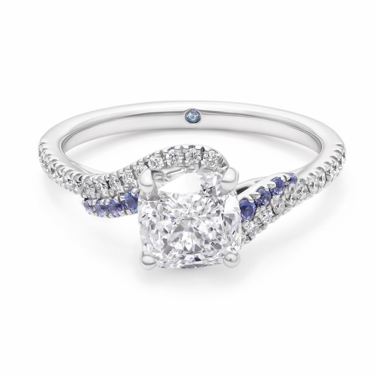 Custom platinum engagement ring with cushion cut diamond centre and asymmetric air current flows swirls in blue sapphire and diamond pave band and basket filigree copy