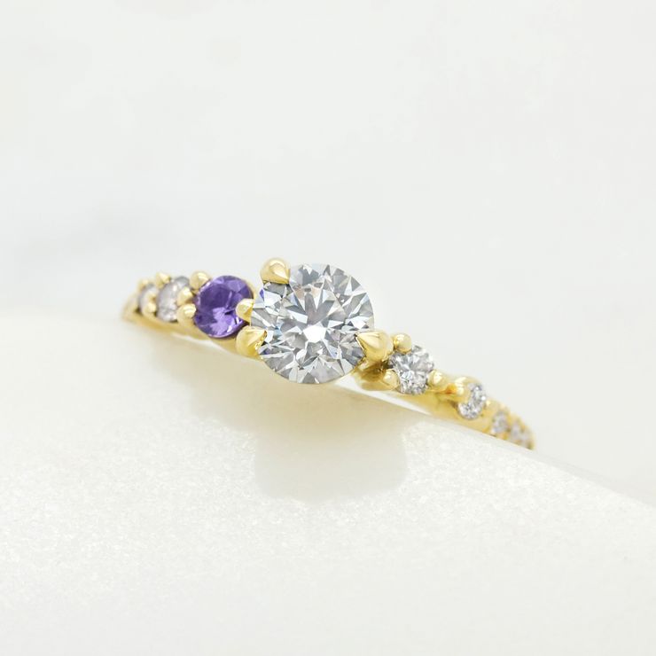 Round brilliant diamond with a purple sapphire accent gemstone set in yellow gold