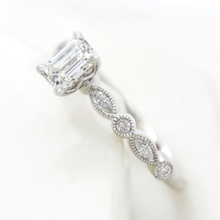 Emerald cut diamond engagement ring with marquise and round diamond milgrain band