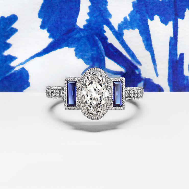 Vintage inspired oval diamond engagement ring with milgrain and flanking blue sapphire baguettes