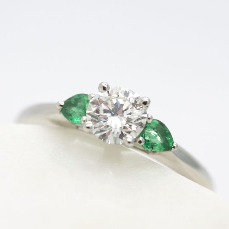 Trilogy engagement ring with round center diamond with emerald pear side stones