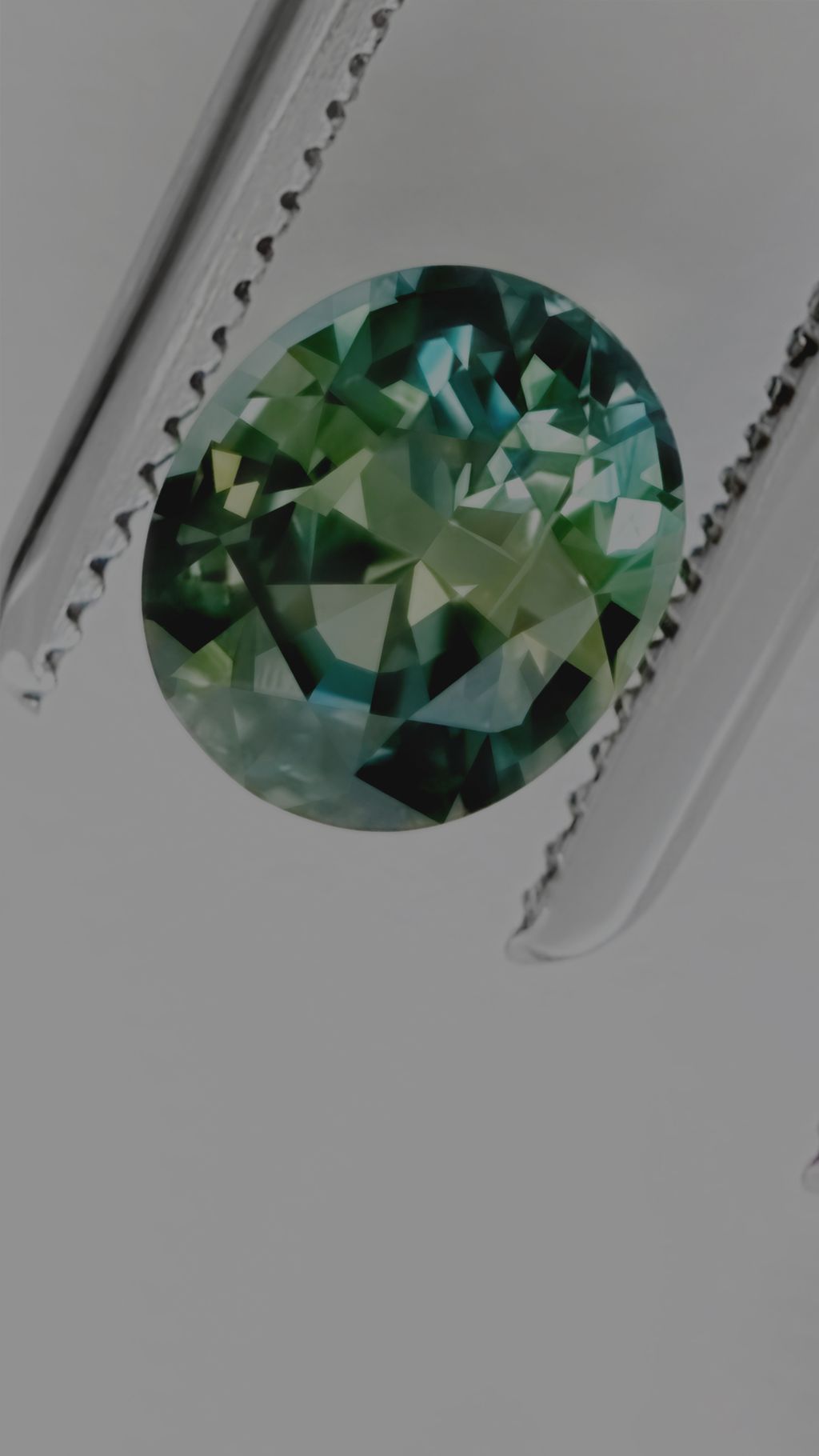 Green sapphire gemstone held in jeweller tweezers